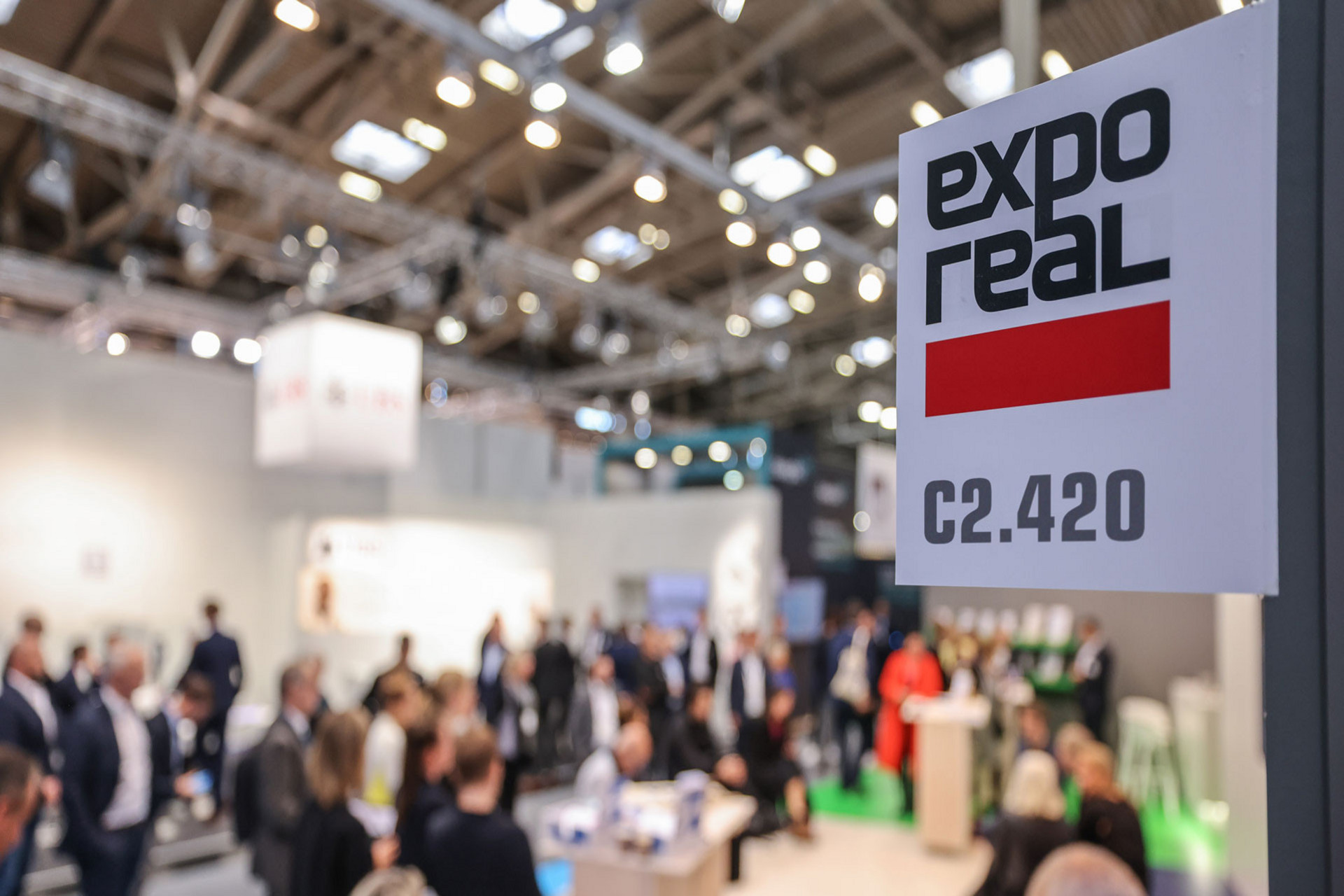 DGNB Standnummer auf der Expo Real mit einem verschwommenen Messestand im Hintergrund